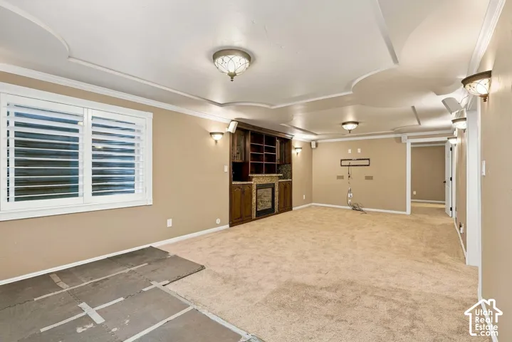 Recessed ceiling with decorative molding, built-in entertainment cabinetry with stone surround, wall sconces, ceiling-mounted light fixtures, and white window shutters
