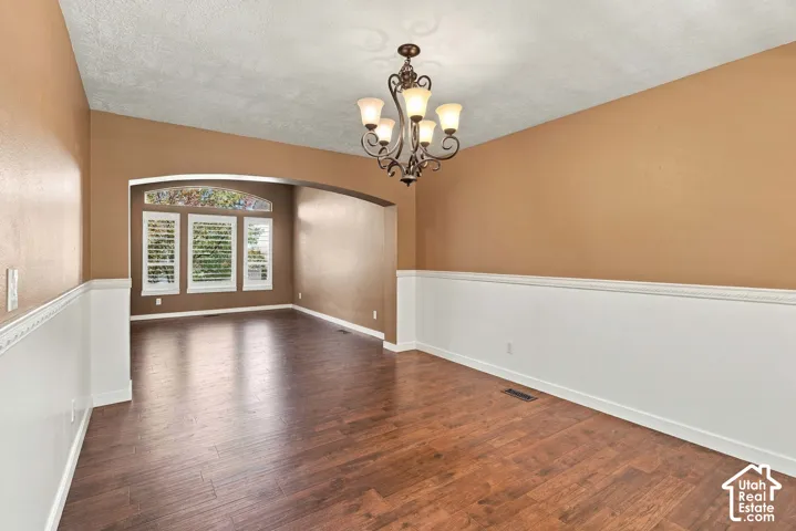 Hardwood-finish flooring, decorative chandelier, arched entryway, wainscoting, and large windows with plantation shutters