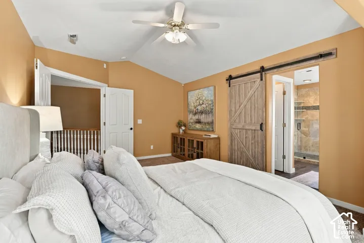 Vaulted ceiling with a ceiling fan, wood-finish barn door, built-in wooden console, and a glass-enclosed shower