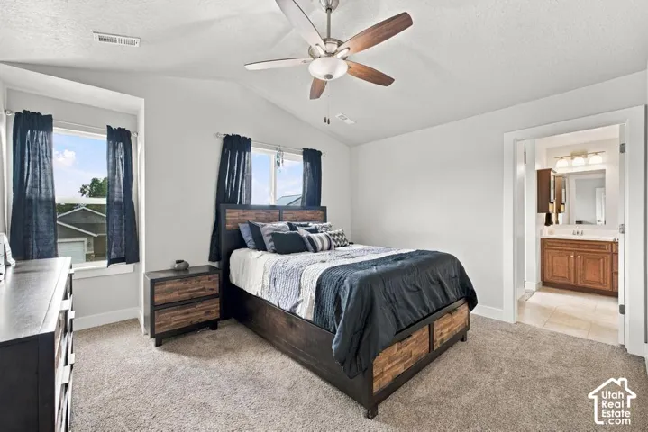 Vaulted ceiling with an attached ceiling fan, dual windows providing ample natural light, and carpeted flooring