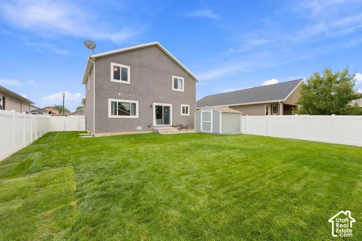 Expansive backyard featuring a manicured lawn, full privacy fencing, and a dedicated storage shed