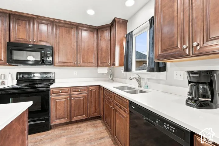 L-shaped kitchen with wood-finish cabinetry, white countertops, a double basin stainless steel sink, and black appliances