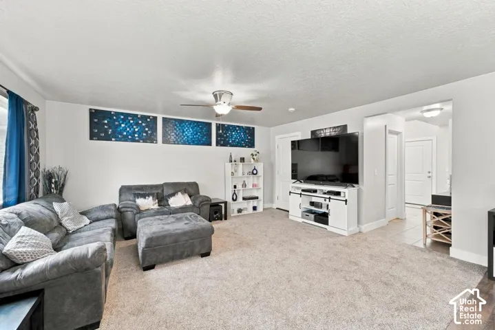 Neutral-toned carpeting, ceiling fan with light fixture, and a white entertainment console with barn door-style accents