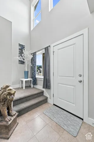 Two-panel entry door, tiled flooring, high ceilings, upper transom windows, and carpeted stairs
