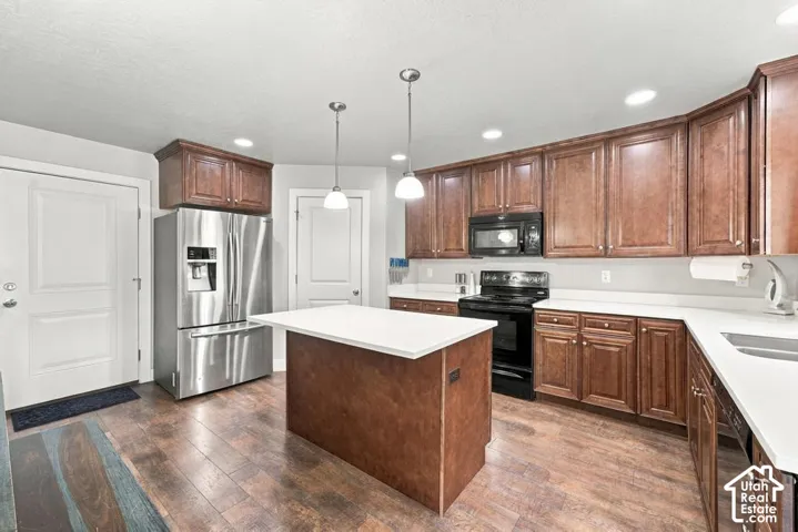 Kitchen featuring wood-finish flooring, a central island with a white countertop, dark wood cabinetry, white countertops, and stainless steel appliances