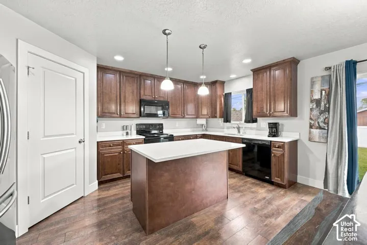 Kitchen featuring wood-finish flooring, dark wood cabinetry, a center island with a light-colored countertop, recessed lighting, and pendant lighting