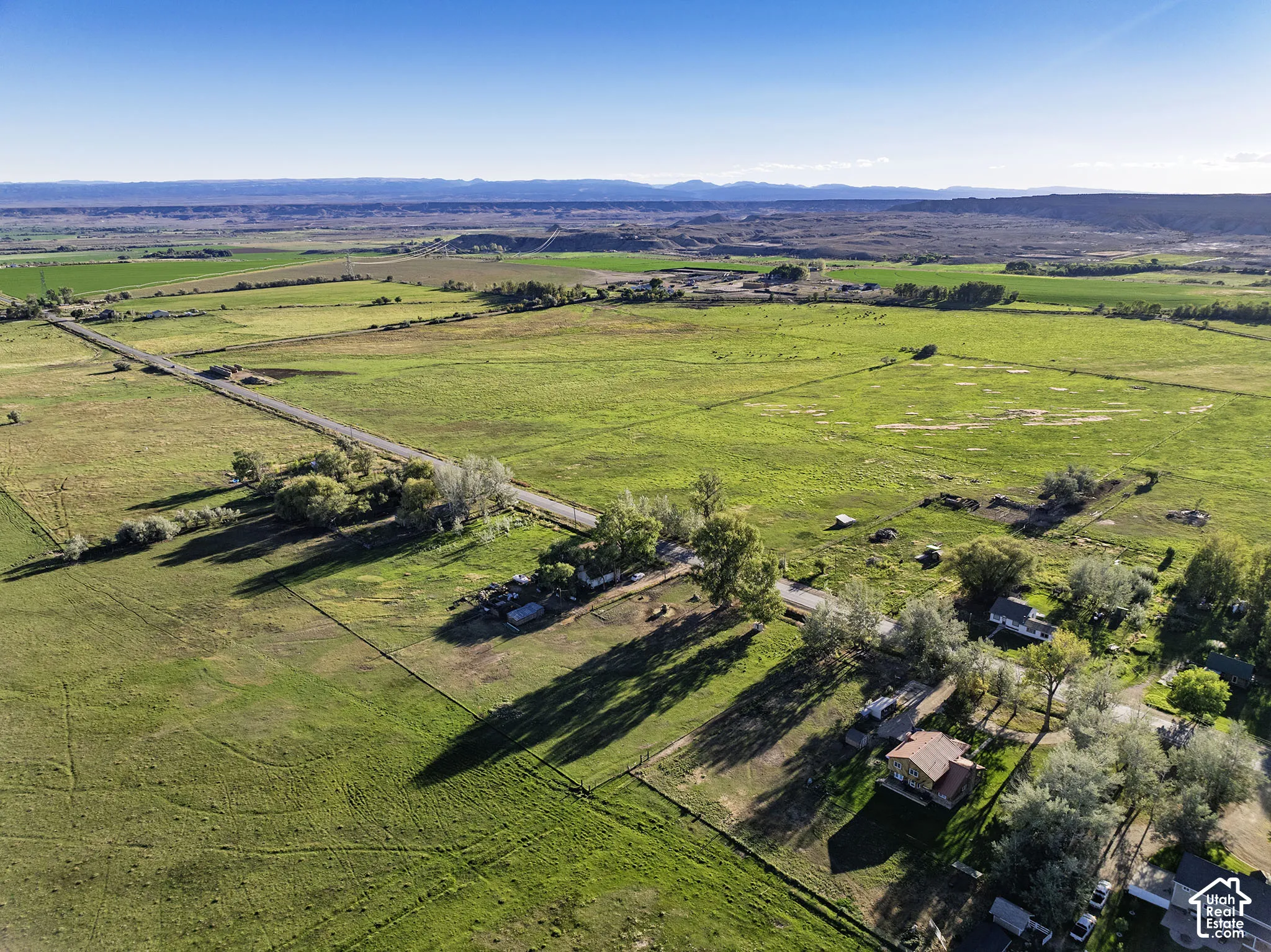 Expansive land with green fields, paved road access, scattered trees, and distant mountain ranges