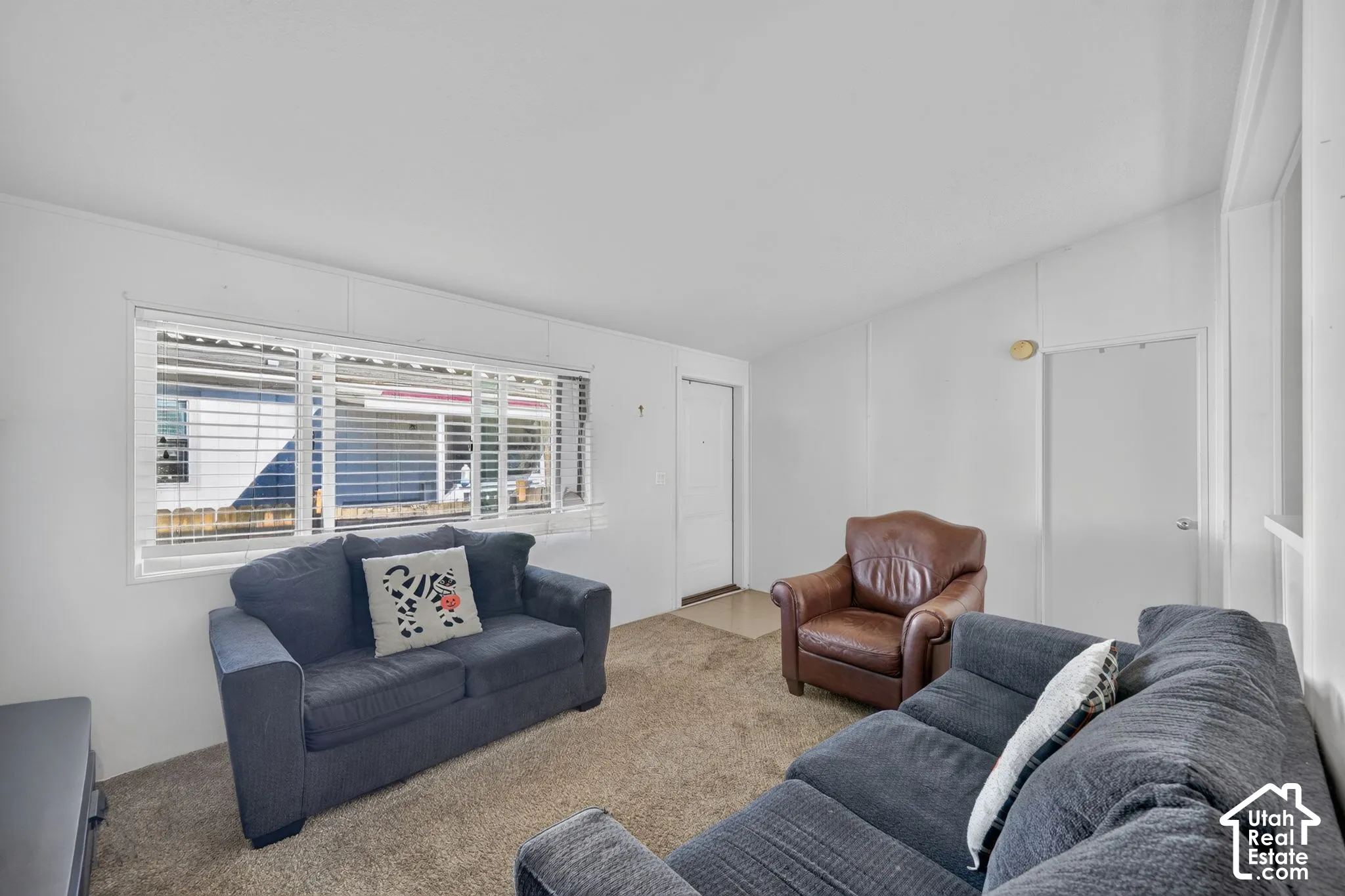 Wall-to-wall carpeting with a front entry door, multiple windows featuring blinds, and an interior door