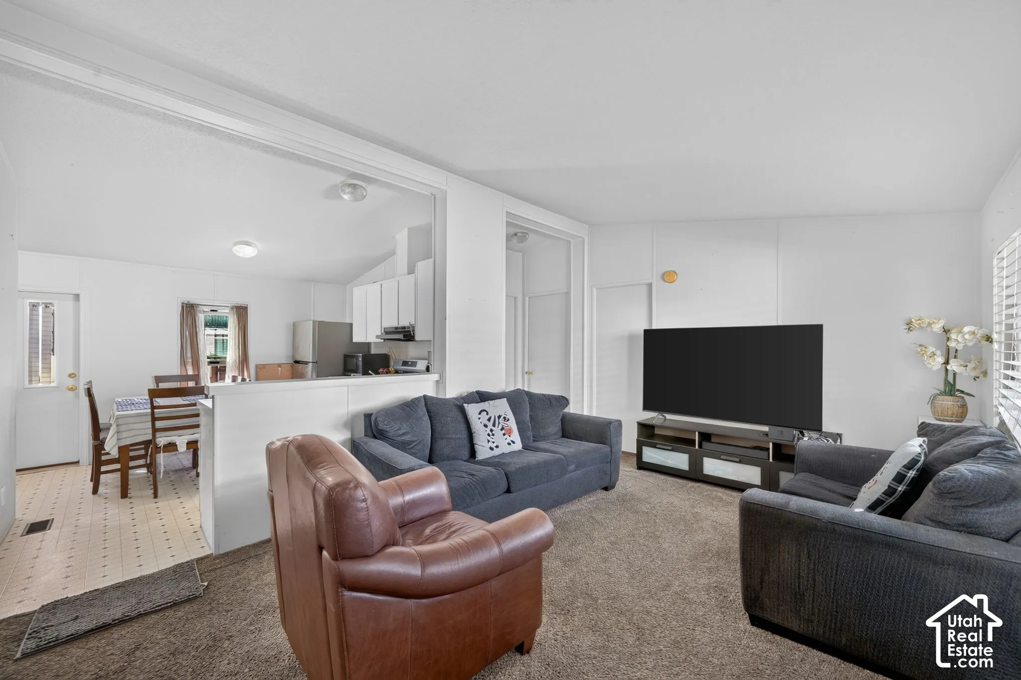 Open-concept living space featuring neutral carpet flooring, white walls, and a large window with blinds