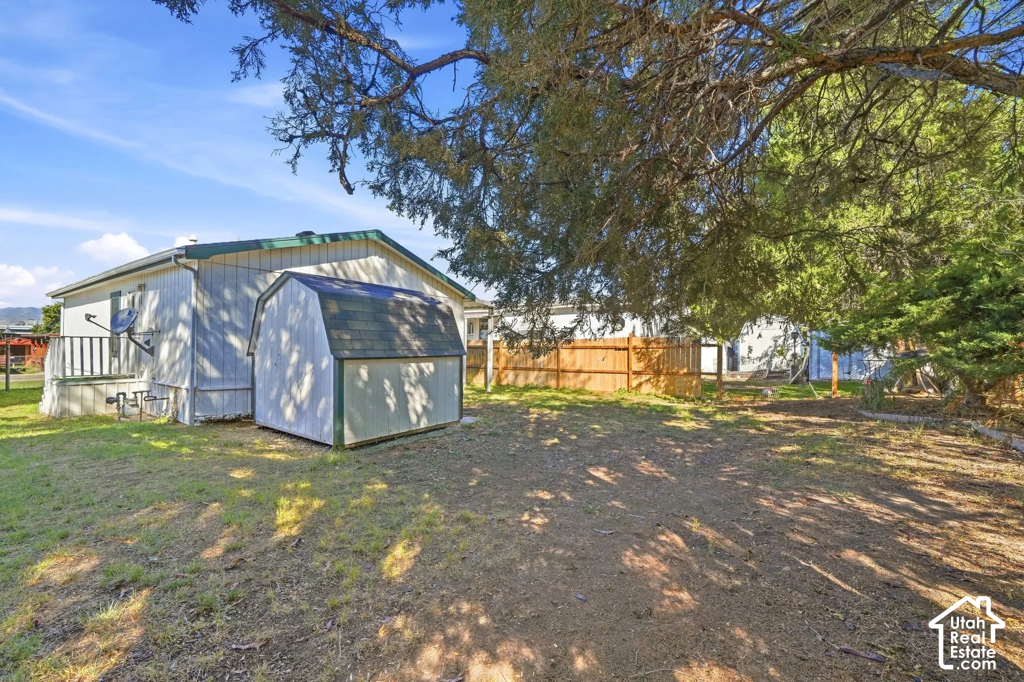 Expansive outdoor area featuring a storage shed with a gambrel roof, mature trees, and a wood privacy fence