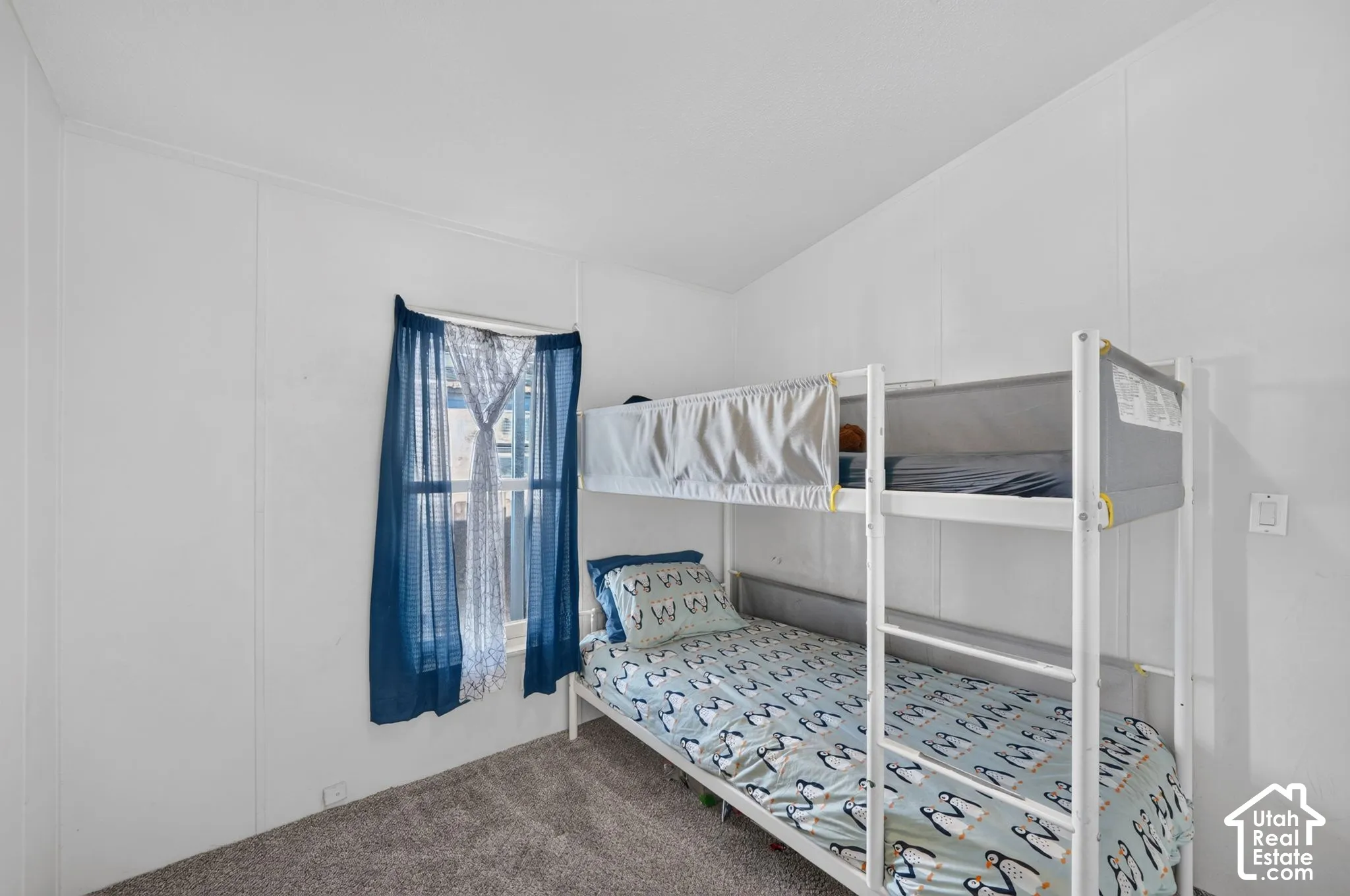 White paneled walls with a window featuring blue drapery, and neutral carpet flooring