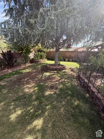 Expansive backyard featuring a mature tree with a stone-edged base, a brick-finish perimeter wall, and established garden beds