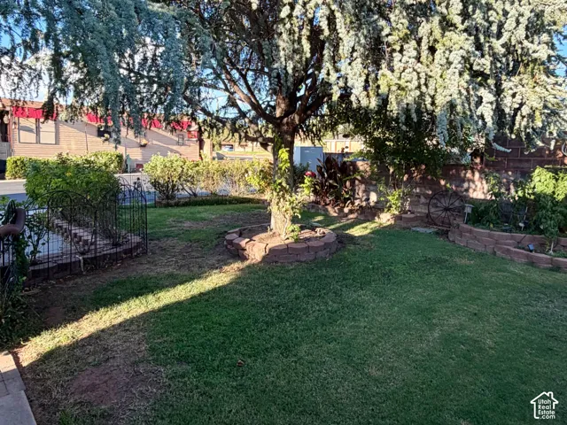 Expansive green lawn, mature shade tree, brick-edged planter beds, and wrought iron fencing