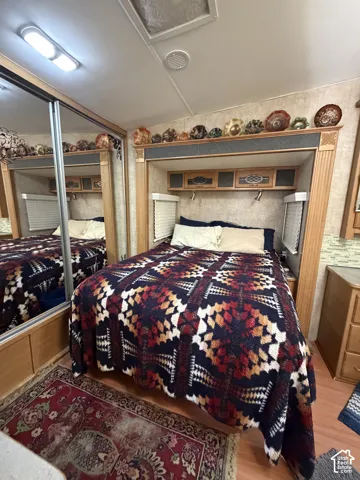 Built-in bed frame with overhead storage, integrated reading lights, sliding mirrored wardrobe, and wood-finish flooring