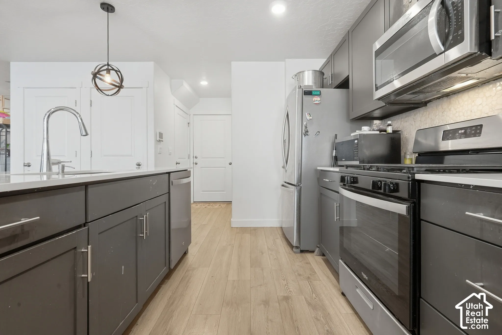 Kitchen featuring wood-finish flooring, stainless steel appliances, dark gray cabinetry, light-toned countertops, and a decorative pendant light fixture