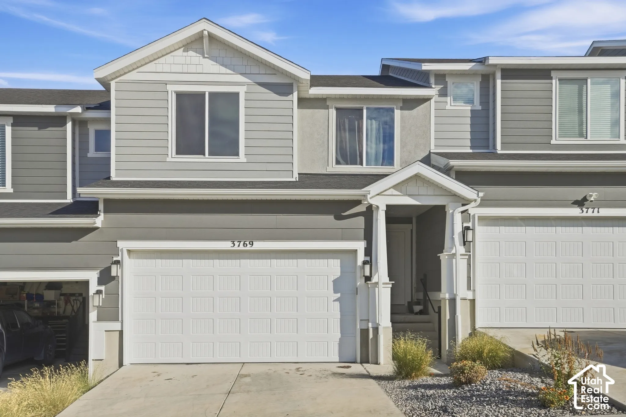 Gray siding exterior with white trim details, featuring a covered front entry, an integrated garage with a panel door, and a paved driveway