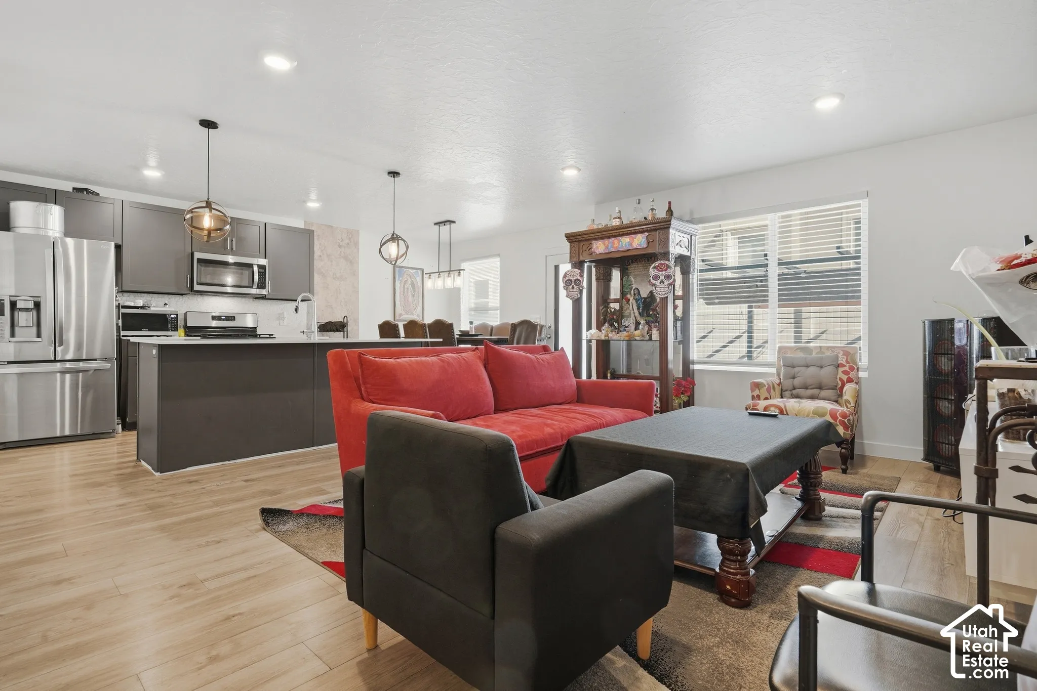 Open-concept living space featuring wood-finish flooring, recessed lighting, and a kitchen with stainless steel appliances, dark cabinetry, and a central island