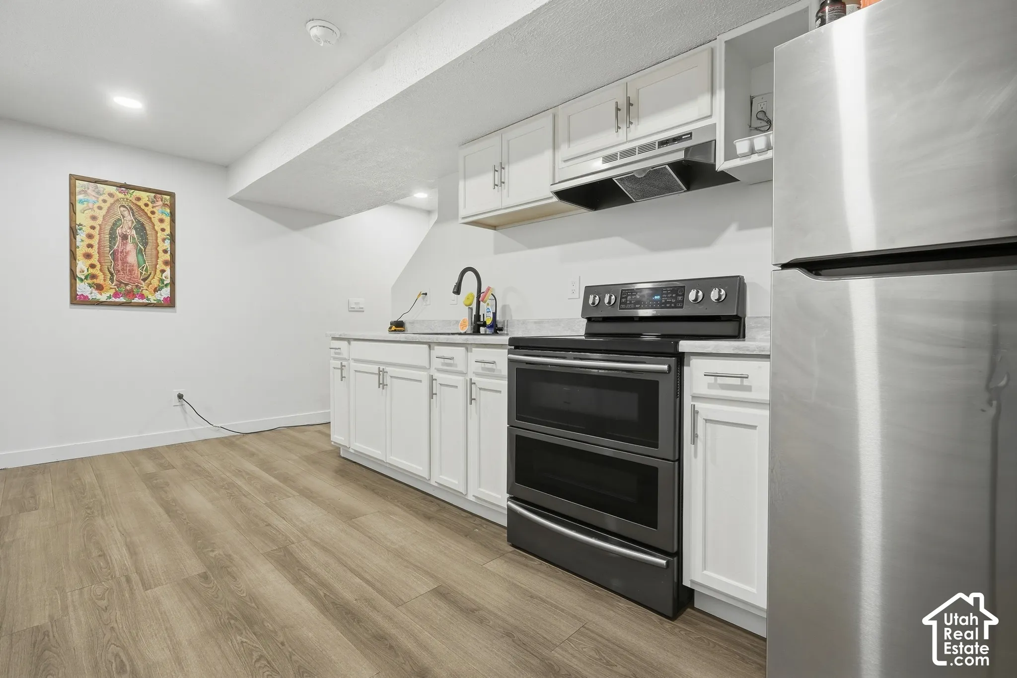 Wood-finish flooring, white cabinetry, granite-style countertops, stainless steel appliances, and recessed lighting