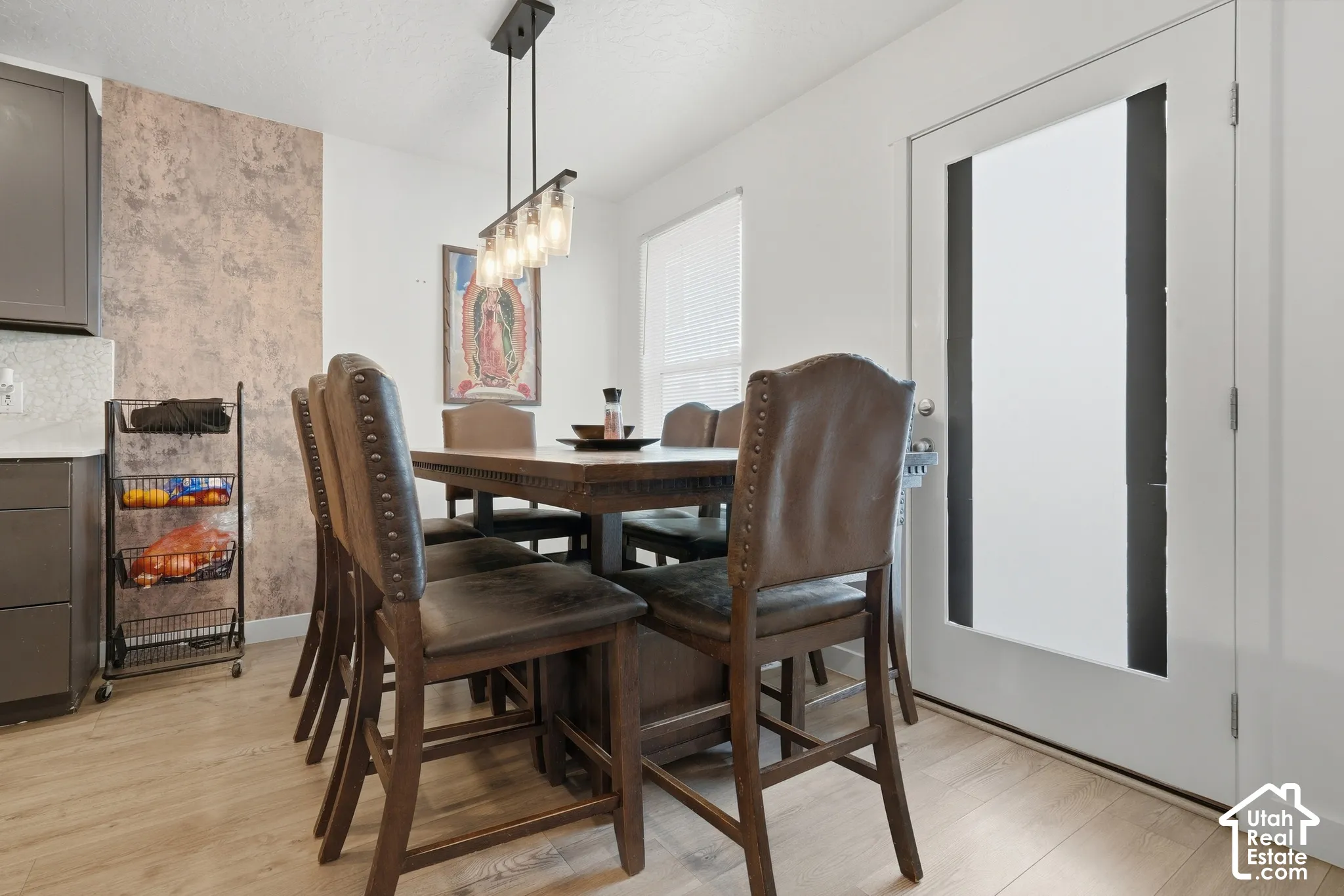 Wood-finish flooring, textured accent wall, sleek linear pendant light fixture, white door with frosted glass panels, and a window with blinds