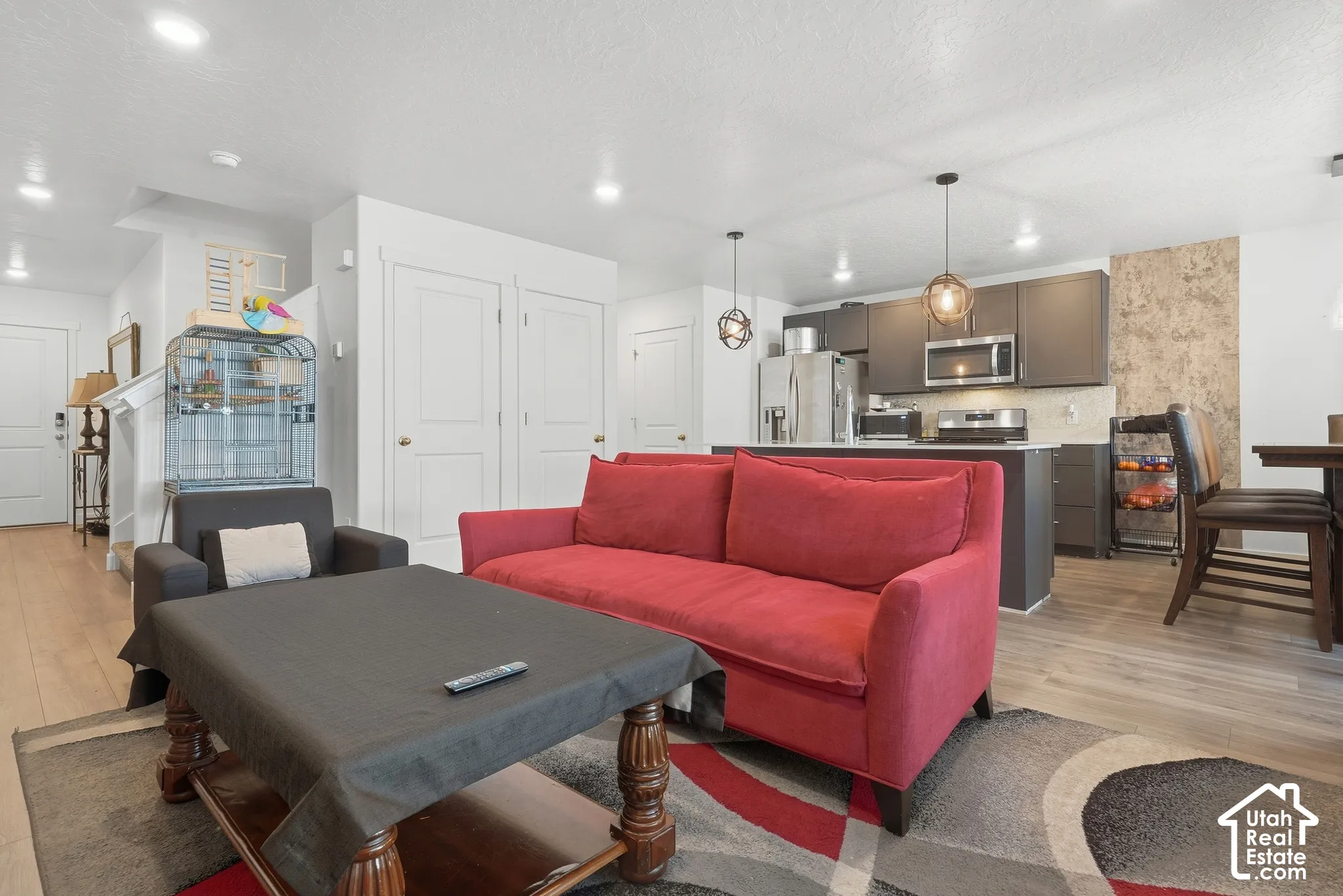 Open-concept living space featuring wood-finish flooring, recessed lighting, and a modern kitchen with dark cabinetry and stainless steel appliances