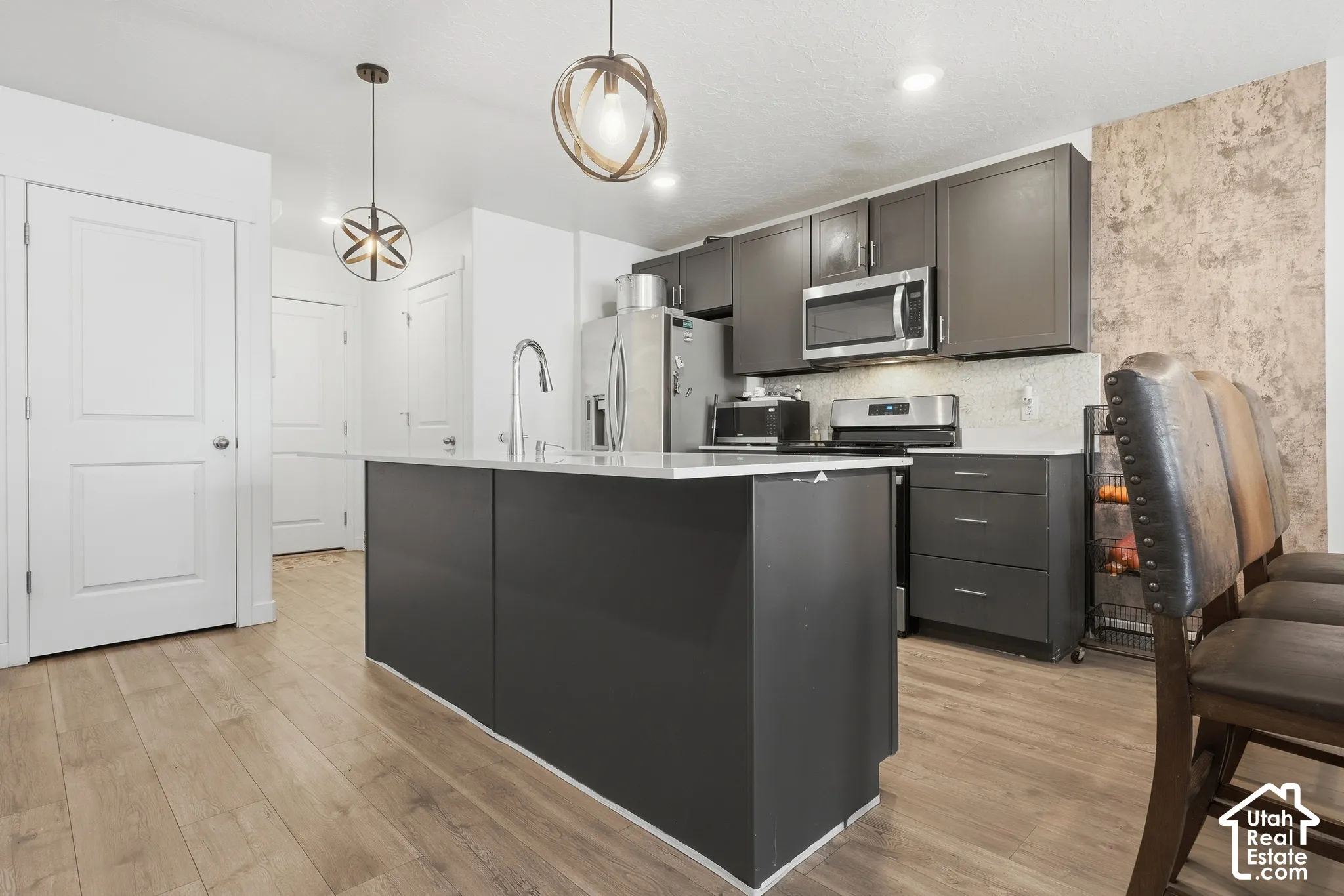 Kitchen featuring an island with a stainless steel faucet, wood-finish flooring, dark cabinetry, and recessed lighting