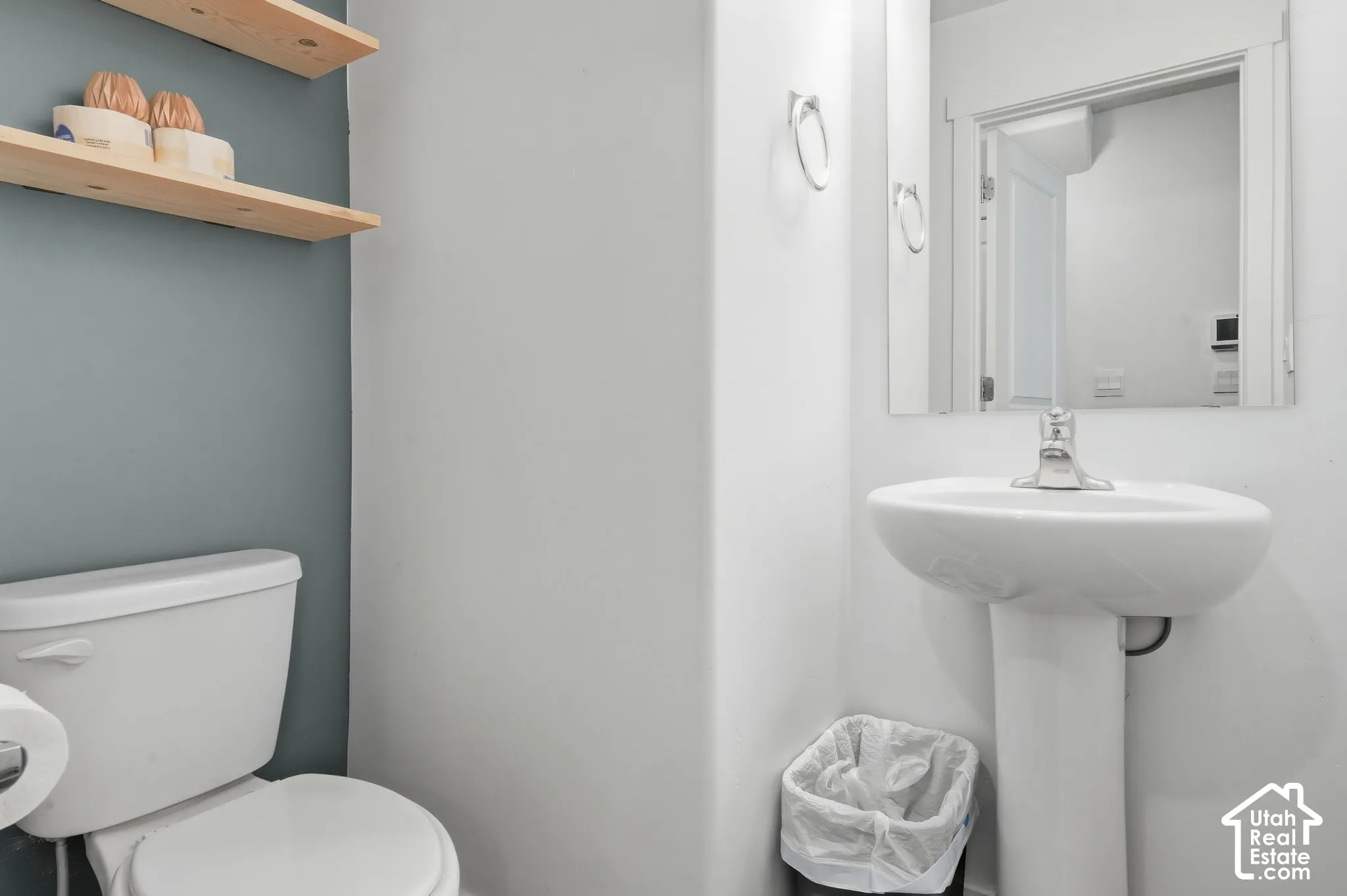 Pedestal sink with chrome faucet, wall-mounted mirror, and white toilet