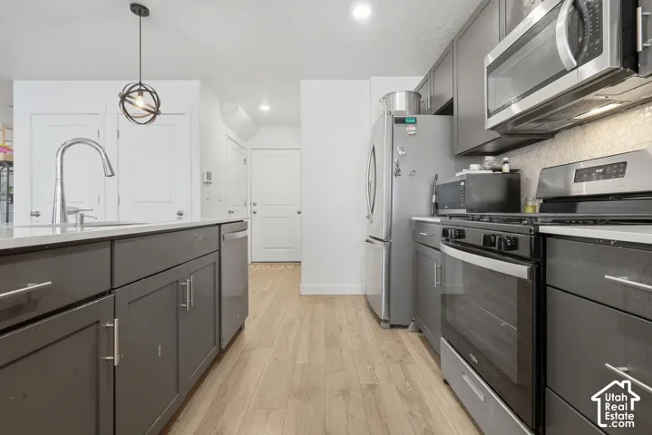 Kitchen featuring wood-finish flooring, stainless steel appliances, dark gray cabinetry, light-toned countertops, and a decorative pendant light fixture