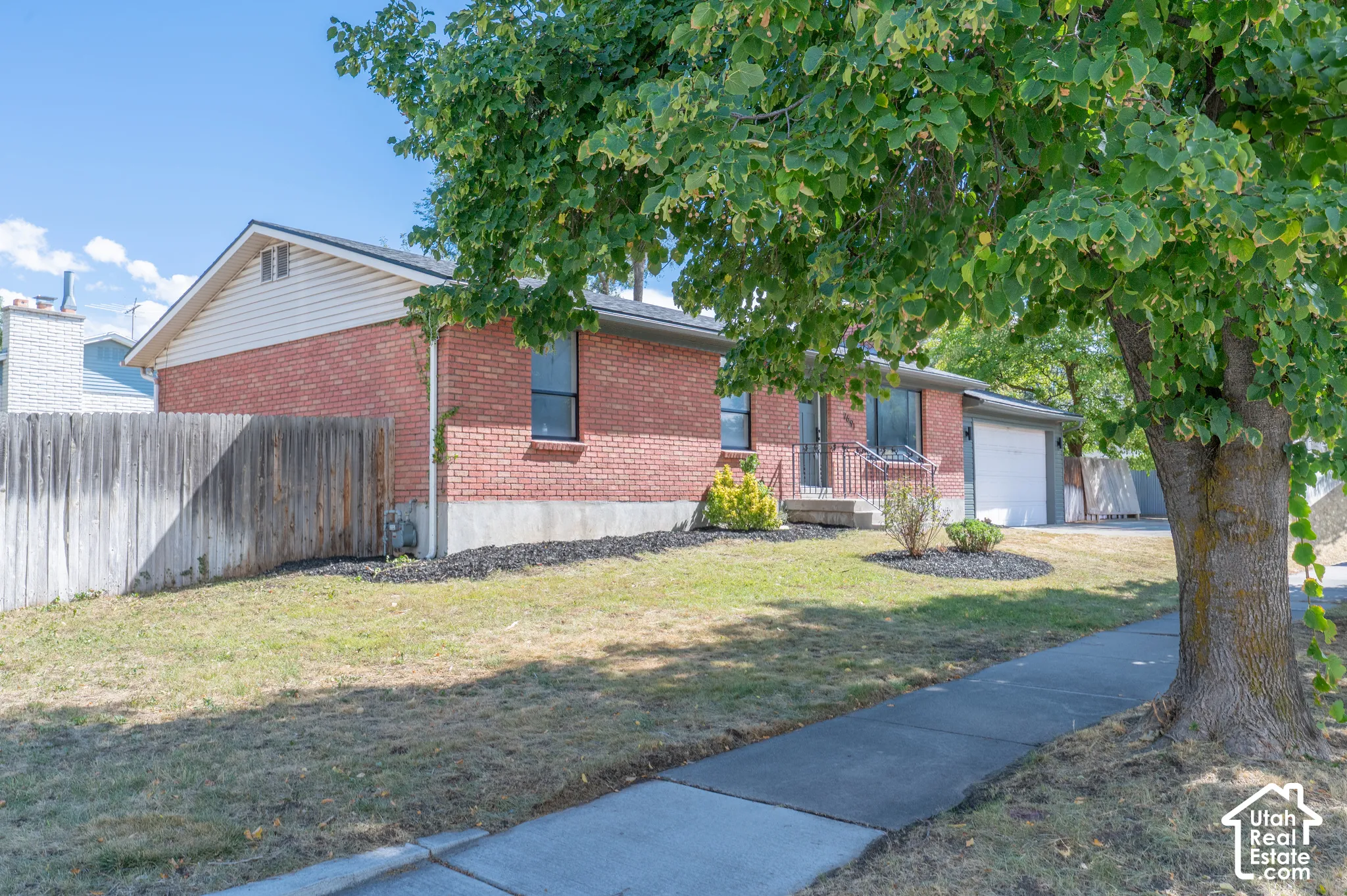 Red brick exterior, attached garage, well-maintained landscaping, privacy fencing, mature tree