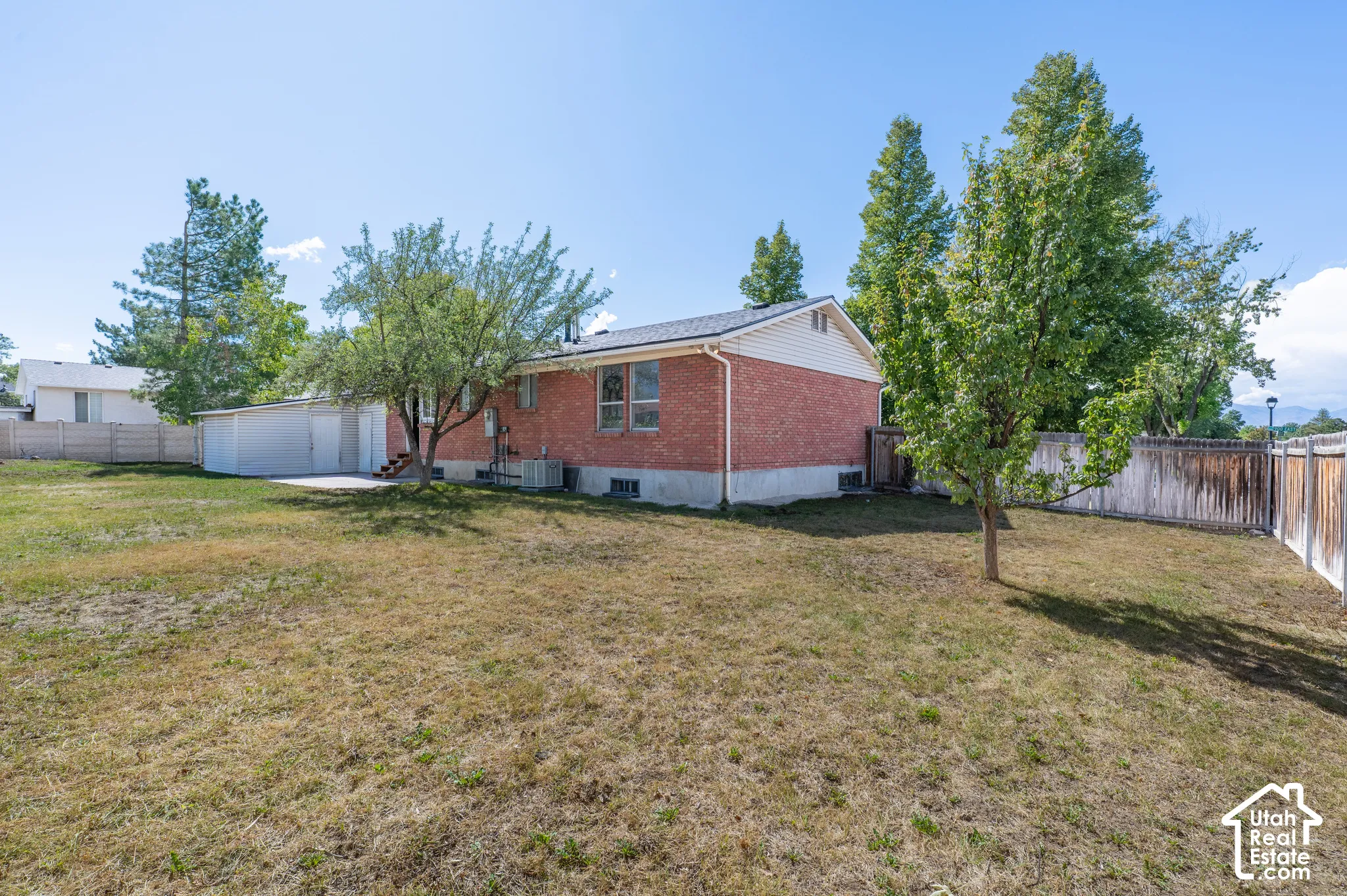Expansive backyard featuring mature trees, a detached garage, and a brick exterior home with a partial fenced perimeter