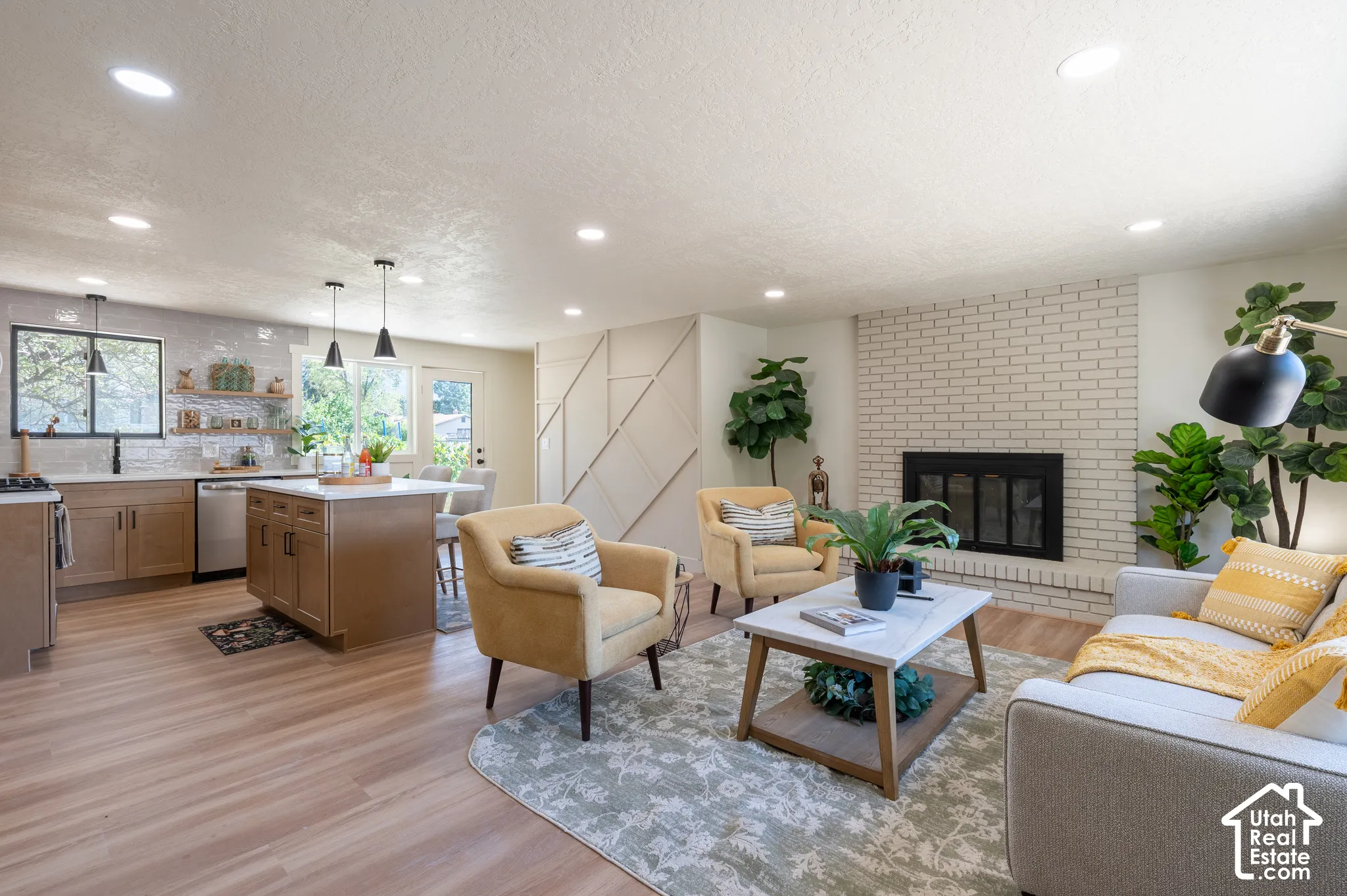 Open-concept living space featuring wood-finish flooring, a kitchen island with seating, a white brick fireplace, recessed lighting, and built-in cabinetry