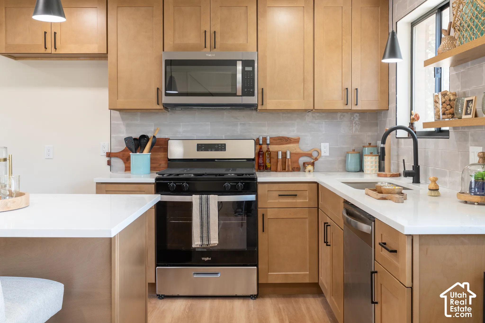 Wood-finish cabinetry, stainless steel appliances, light-toned countertops, a matte black faucet, and a tiled backsplash