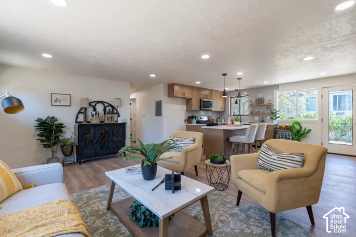 Open-concept living space featuring wood-finish flooring, recessed lighting, and a modern kitchen with a central island and pendant lighting