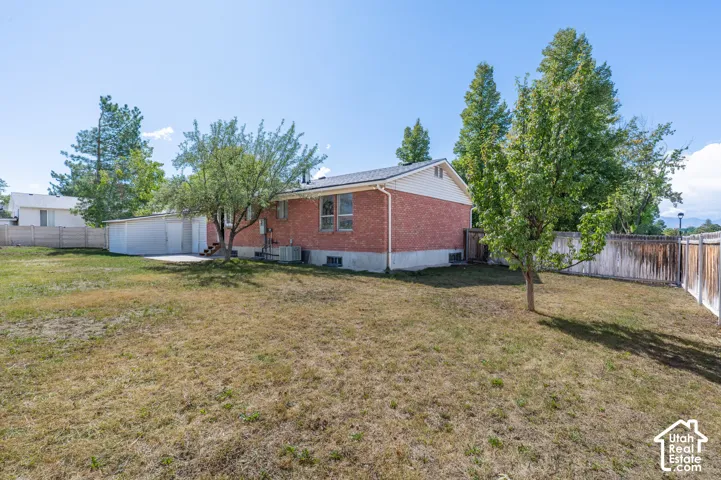 Expansive backyard featuring mature trees, a detached garage, and a brick exterior home with a partial fenced perimeter