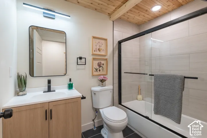 Wood-finish ceiling with exposed beams, white tile shower surround, black-framed sliding glass shower door, light wood-finish vanity with white countertop, and black-finish fixtures
