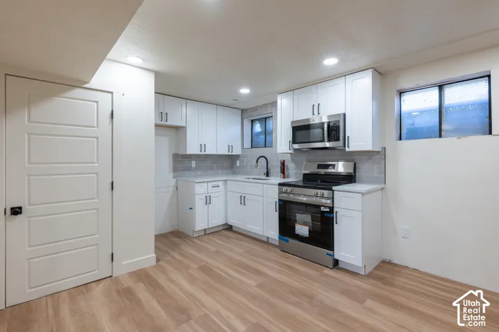 Contemporary kitchen featuring white cabinetry, stainless steel appliances, solid surface countertops, a tile backsplash, and wood-finish flooring