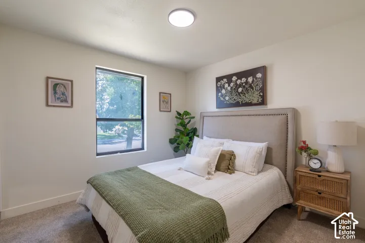 Neutral wall paint, plush carpet flooring, large window with natural light, modern ceiling light fixture, and a built-in upholstered headboard