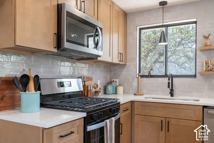 Light wood-finish cabinetry, white countertops, subway tile backsplash, stainless steel appliances, and a modern pendant light fixture