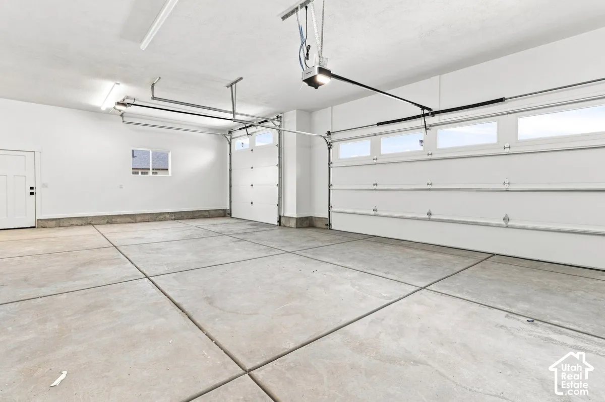 Concrete flooring, two automatic garage doors with upper window panels, white walls, and fluorescent lighting