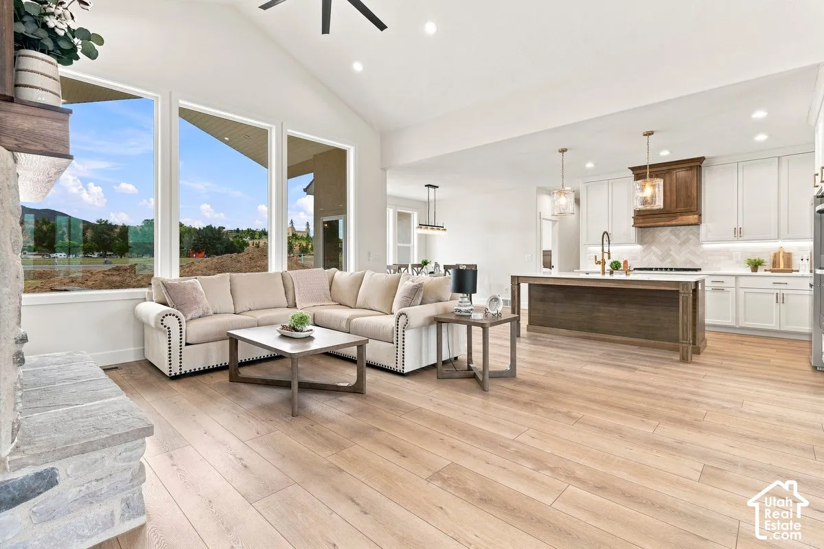 Vaulted ceiling, recessed lighting, wood-finish flooring, stone fireplace, and kitchen island with pendant lighting