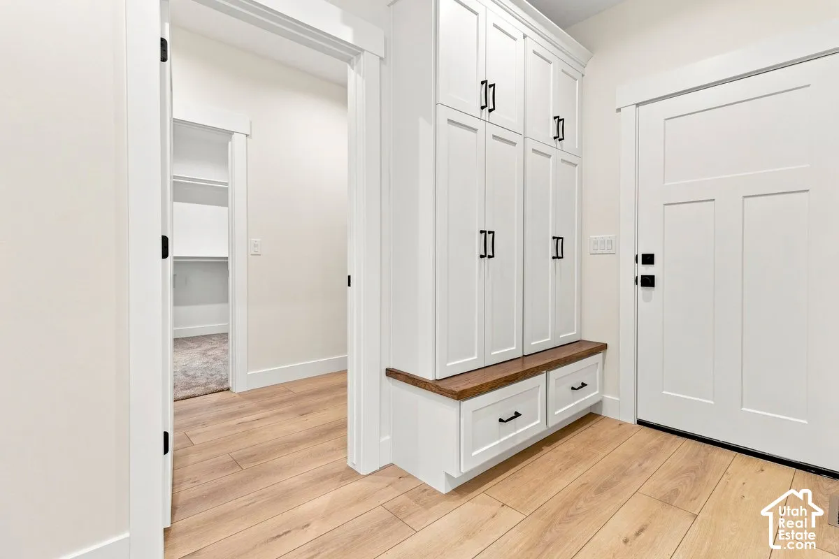 Wood-finish flooring, built-in white cabinetry, storage bench with wood-finish top, white paneled door, and black hardware accents