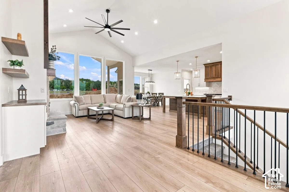 Vaulted ceilings with recessed lighting, large picture windows, wood-finish flooring, staircase with wood banister and black spindles, and a kitchen featuring wood cabinetry and pendant lighting