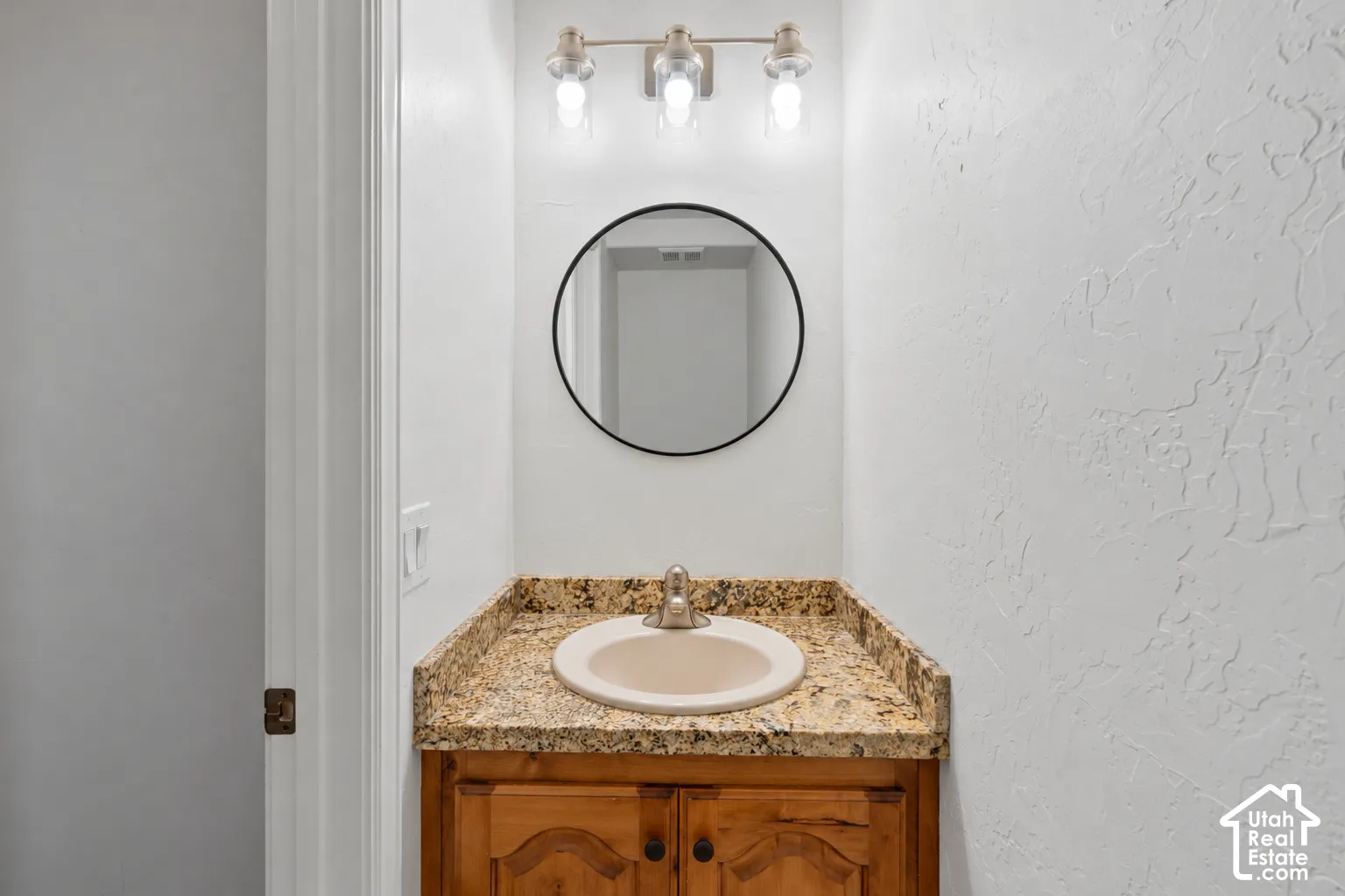 Vanity with a neutral-toned basin, a decorative mirror, and a three-light fixture