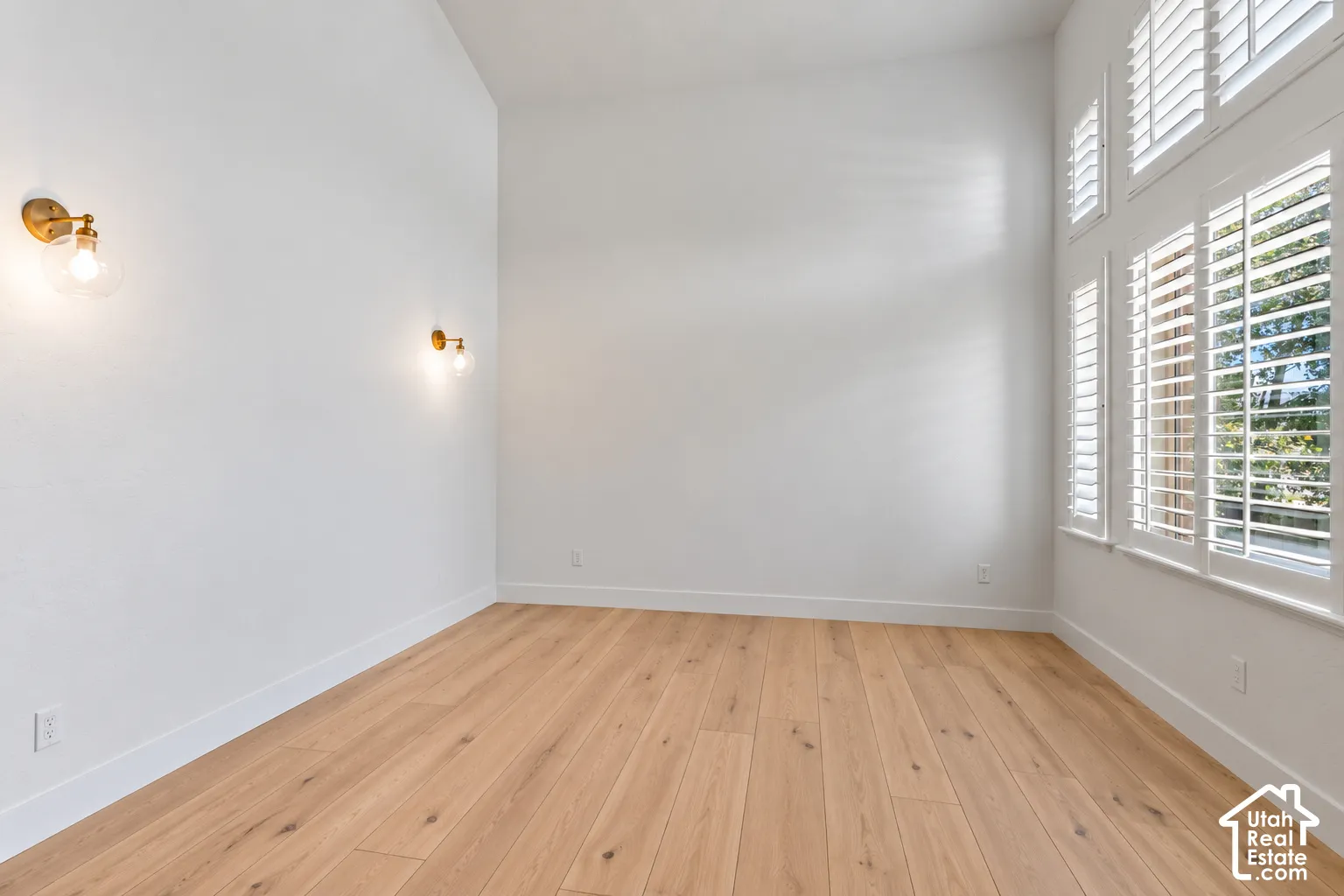 High ceilings featuring brass sconces and light wood-finish flooring