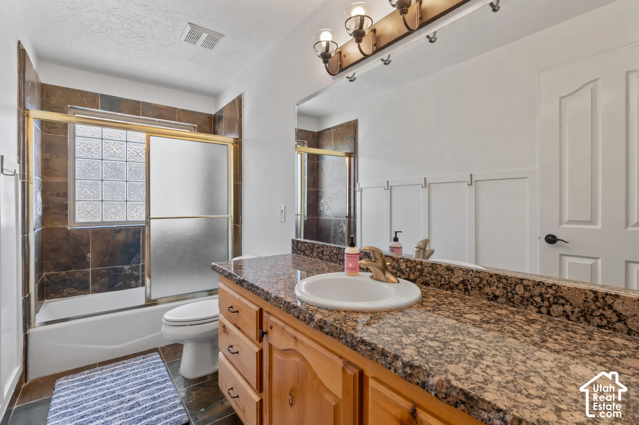 Granite-finish countertop with an integrated sink, wood-finish vanity, and a tiled shower-tub combination with glass block window accents