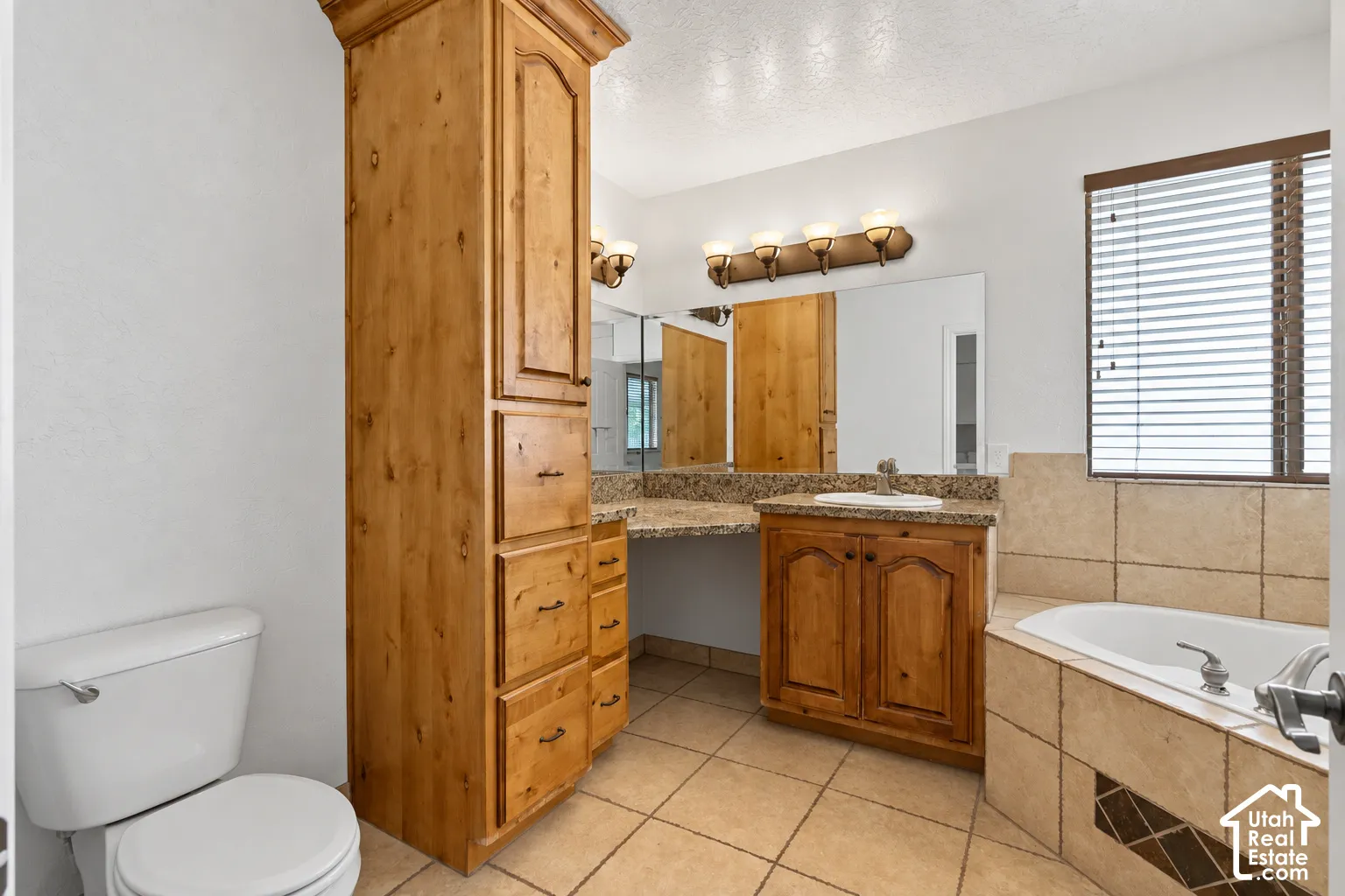 Bathroom featuring a built-in soaking tub, tile flooring, wood-finish cabinetry, and a vanity with a stone countertop
