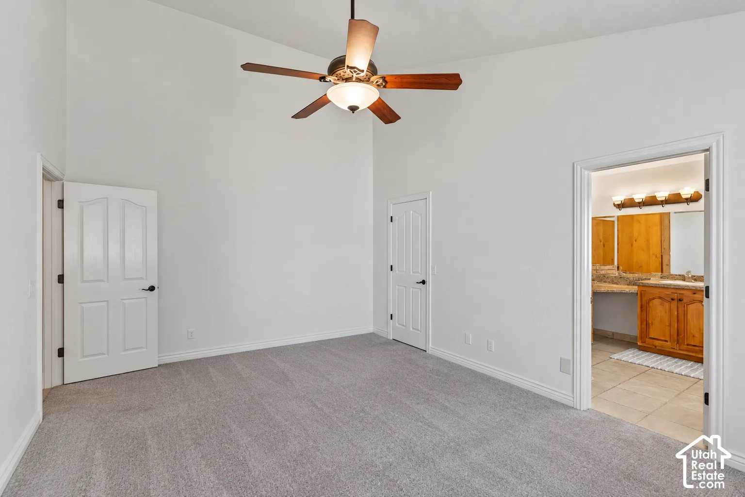 Vaulted ceiling with a wood-finish ceiling fan, neutral carpet, and two-panel interior doors