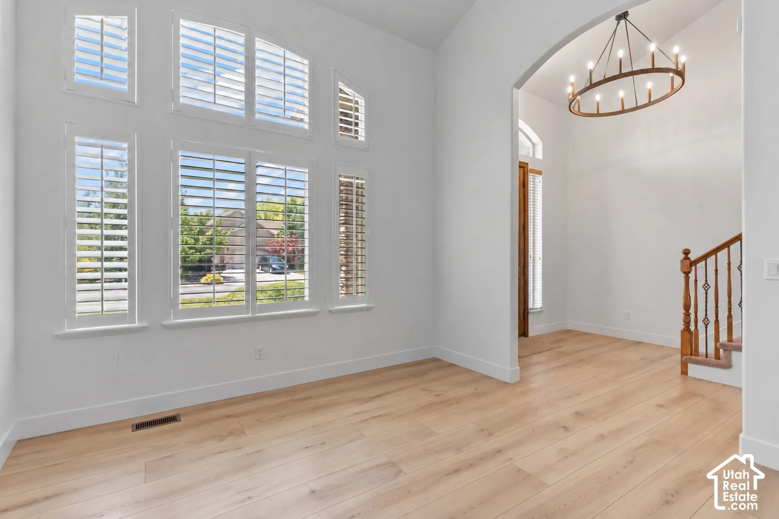 Vaulted ceiling, wood-finish flooring, custom window shutters, arched doorway, and a decorative chandelier