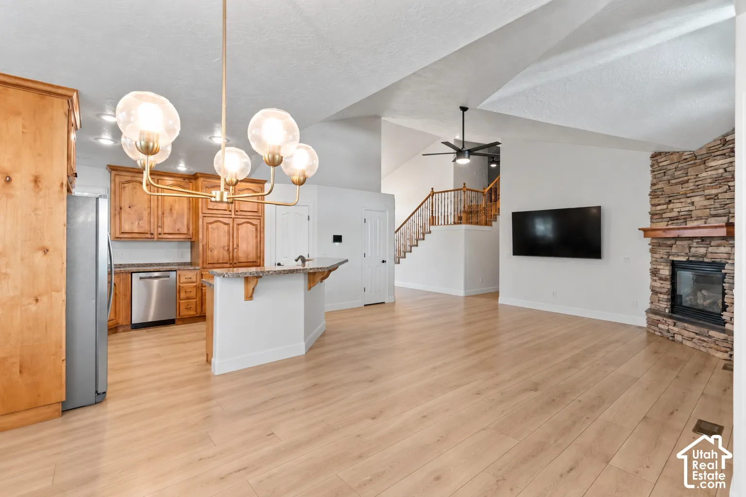 Spacious interior featuring wood-finish flooring, a stone-clad fireplace, and a kitchen with wood cabinetry and stainless steel appliances