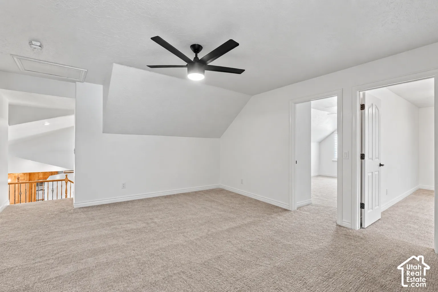 Expansive carpeted space featuring a modern black ceiling fan with integrated lighting