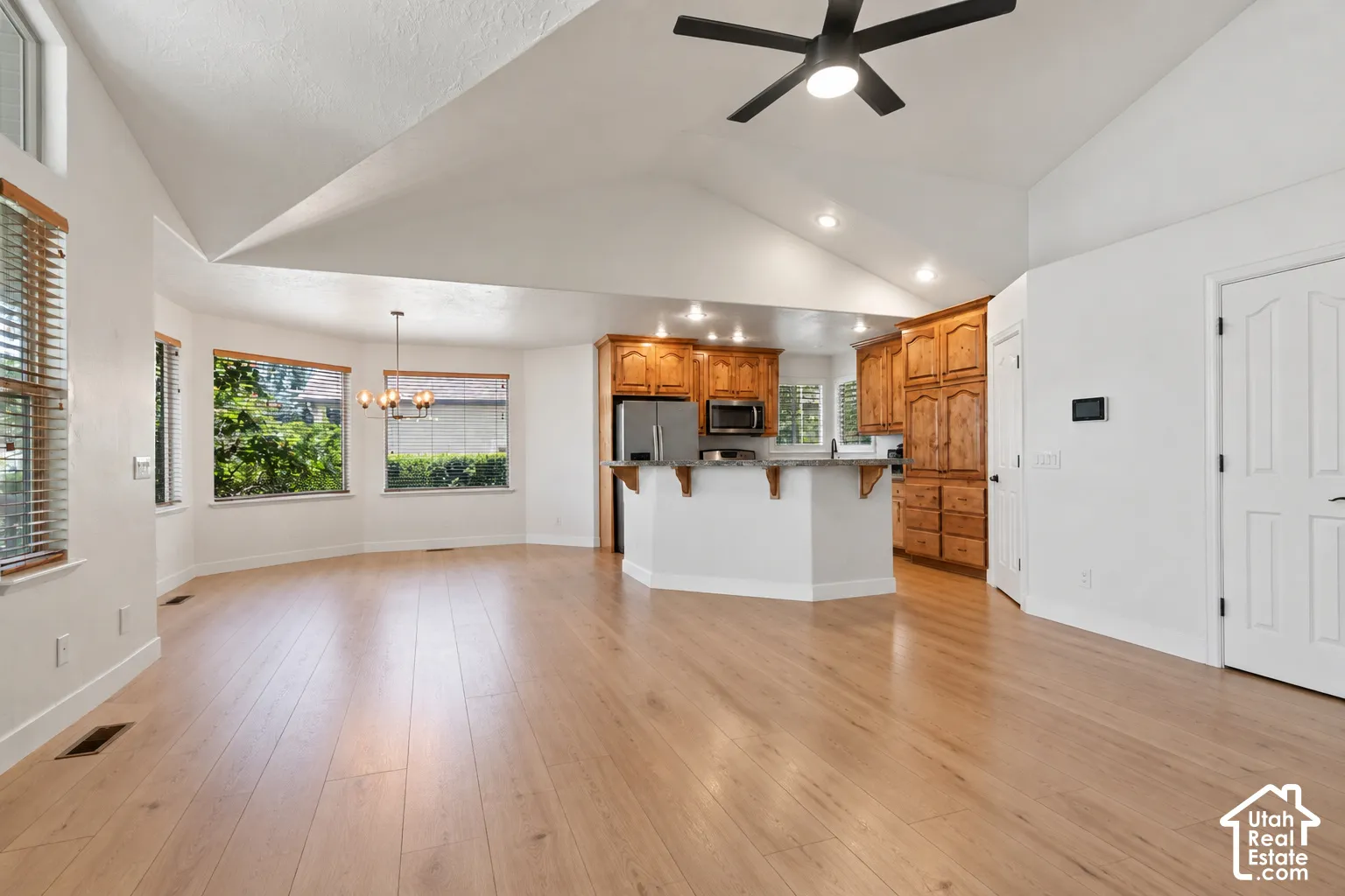 Vaulted ceiling with a black ceiling fan, wood-finish flooring, recessed lighting, and a kitchen featuring wood cabinetry and stainless steel appliances